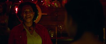 Movie still from “Summering” (2022), directed by James Ponsoldt – A woman smiling at the camera in front of some lights; Close Up shot, Over the shoulder angle