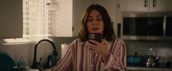 Movie still from “Summering” (2022), directed by James Ponsoldt – A woman looking at her cell phone in the mirror; Medium shot, Over the shoulder angle