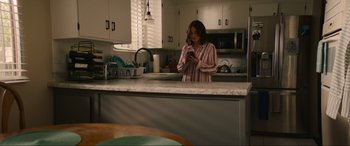 Movie still from “Summering” (2022), directed by James Ponsoldt – A woman standing in a kitchen looking at her cell phone; Medium shot, High angle