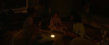 Movie still from “Summering” (2022), directed by James Ponsoldt – A group of people sitting in a circle around a candle; Medium shot, High angle