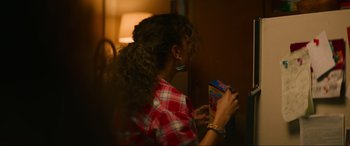 Movie still from “Summering” (2022), directed by James Ponsoldt – A woman holding a box of cereal in her hands; Medium shot, Over the shoulder angle