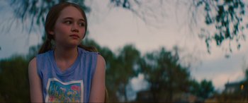 Movie still from “Summering” (2022), directed by James Ponsoldt – A young girl sitting in a chair in front of a tree; Close Up shot, Over the shoulder angle
