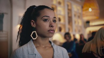 Movie still from “Summertime” (2020), directed by Carlos López Estrada – A young woman with long black hair wearing a white shirt and gold earrings; Close Up shot, Low angle