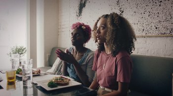 Movie still from “Summertime” (2020), directed by Carlos López Estrada – Two women sitting in front of a plate of food; Medium shot, Over the shoulder angle