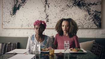 Movie still from “Summertime” (2020), directed by Carlos López Estrada – Two women sitting at a table with plates of food in front of them; Medium shot, Over the shoulder angle