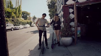 Movie still from “Summertime” (2020), directed by Carlos López Estrada – A man and a woman standing next to a scooter on the side of the street; Wide shot, High angle