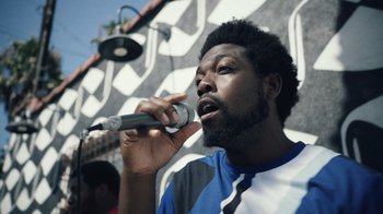 Movie still from “Summertime” (2020), directed by Carlos López Estrada – A man is holding a microphone up to his mouth; Close Up shot, Low angle