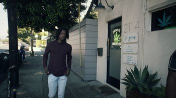 Movie still from “Summertime” (2020), directed by Carlos López Estrada – A man walking down the sidewalk in front of a building; Wide shot, Low angle