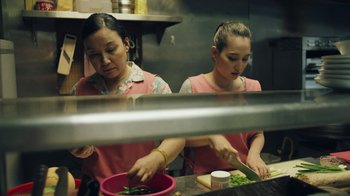 Movie still from “Summertime” (2020), directed by Carlos López Estrada – A couple of women standing in a kitchen preparing food; Medium shot, High angle