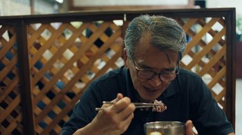 Movie still from “Summertime” (2020), directed by Carlos López Estrada – An older man eating food with chopsticks in a restaurant; Close Up shot, Low angle