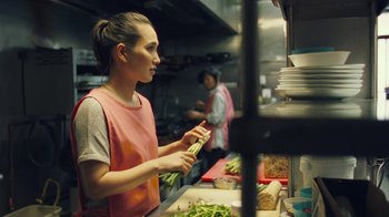 Movie still from “Summertime” (2020), directed by Carlos López Estrada – A woman in a kitchen preparing food in a restaurant; Close Up shot, Over the shoulder angle