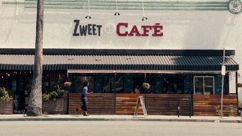 Movie still from “Summertime” (2020), directed by Carlos López Estrada – A woman walking down the sidewalk in front of a cafe; Wide shot, High angle