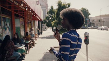 Movie still from “Summertime” (2020), directed by Carlos López Estrada – A person with a cell phone on the sidewalk; Medium shot, Over the shoulder angle