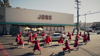 Movie still from “Summertime” (2020), directed by Carlos López Estrada – A group of people in red dresses are marching down the street; Extreme Wide shot, High angle