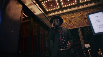 Movie still from “Summertime” (2020), directed by Carlos López Estrada – A man wearing a suit and tie talking on a cell phone; Medium shot, Low angle