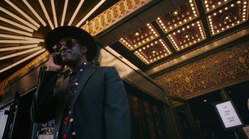 Movie still from “Summertime” (2020), directed by Carlos López Estrada – A man in a suit and hat talking on a phone; Medium shot, Low angle