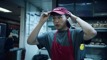 Movie still from “Summertime” (2020), directed by Carlos López Estrada – A man in a red hat and apron putting on a hat; Close Up shot, Over the shoulder angle