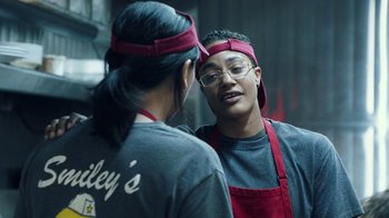 Movie still from “Summertime” (2020), directed by Carlos López Estrada – Two people wearing red aprons talking to each other; Medium shot, Low angle