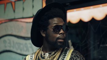Movie still from “Summertime” (2020), directed by Carlos López Estrada – A man wearing a hat and sunglasses with chains around his neck; Close Up shot, Low angle