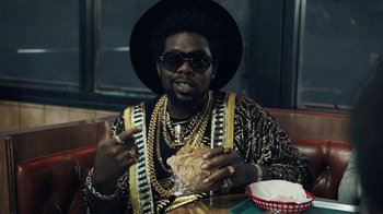 Movie still from “Summertime” (2020), directed by Carlos López Estrada – A man in a black hat eating a sandwich; Medium shot, Overhead angle