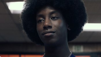 Movie still from “Summertime” (2020), directed by Carlos López Estrada – A young man with a large black afro is smiling for the camera; Close Up shot, Low angle