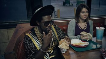 Movie still from “Summertime” (2020), directed by Carlos López Estrada – A man sitting at a table eating a sandwich; Medium shot, Over the shoulder angle