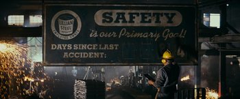 Movie still from “Super 8” (2011), directed by J.J. Abrams – A man in a yellow hard hat standing in front of a sign that says " safety is our primary concern "; Extreme Wide shot, Low angle
