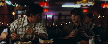 Movie still from “Super 8” (2011), directed by J.J. Abrams – Two people sitting at a table in front of a plate of food; Medium shot, Over the shoulder angle