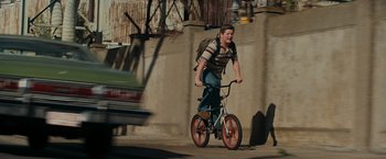 Movie still from “Super 8” (2011), directed by J.J. Abrams – A man riding a bike down a street with a back pack on; Wide shot, Low angle
