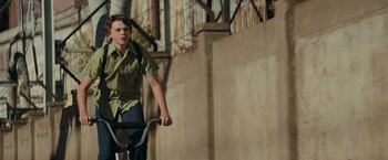 Movie still from “Super 8” (2011), directed by J.J. Abrams – A man riding a bike down a street; Medium shot, Low angle