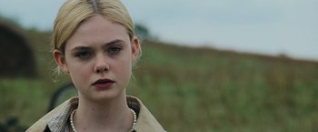 Movie still from “Super 8” (2011), directed by J.J. Abrams – A young woman with a pearl necklace stands in front of a grassy field; Close Up shot, Over the shoulder angle