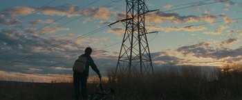 Movie still from “Super 8” (2011), directed by J.J. Abrams – A person riding a bike in a field near a power line; Extreme Wide shot, Low angle