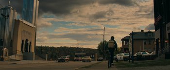 Movie still from “Super 8” (2011), directed by J.J. Abrams – A man riding a bike down a street with cars in the background; Extreme Wide shot, Low angle