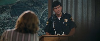 Movie still from “Super 8” (2011), directed by J.J. Abrams – A police officer is speaking at a press conference; Medium shot, Over the shoulder angle