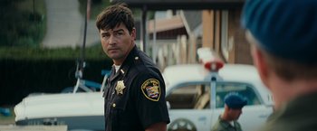Movie still from “Super 8” (2011), directed by J.J. Abrams – A man in a police uniform standing in front of cars; Close Up shot, Over the shoulder angle