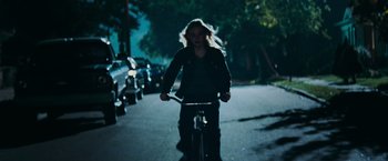 Movie still from “Super 8” (2011), directed by J.J. Abrams – A woman riding a bike down a street at night; Wide shot, High angle