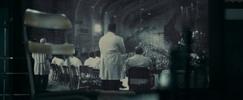 Movie still from “Super 8” (2011), directed by J.J. Abrams – A group of people sitting in a large room; Extreme Wide shot, Over the shoulder angle