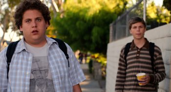 Movie still from “Superbad” (2007), directed by Greg Mottola – Two young men walking down a sidewalk with backpacks on; Medium shot, Over the shoulder angle