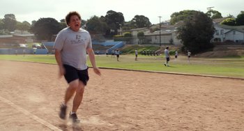 Movie still from “Superbad” (2007), directed by Greg Mottola – A man running across a dirt field with other people in the background; Wide shot, Low angle