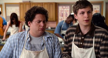 Movie still from “Superbad” (2007), directed by Greg Mottola – Two men in aprons in a kitchen with other people in the background; Medium shot, Over the shoulder angle