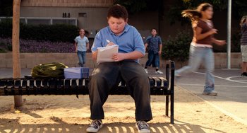 Movie still from “Superbad” (2007), directed by Greg Mottola – A boy sitting on top of a bench writing on a piece of paper; Wide shot, High angle
