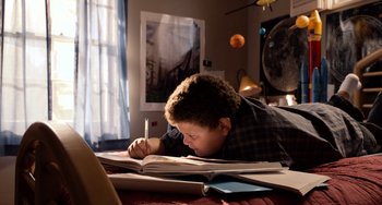 Movie still from “Superbad” (2007), directed by Greg Mottola – A young boy is writing on a book; Wide shot, Overhead angle
