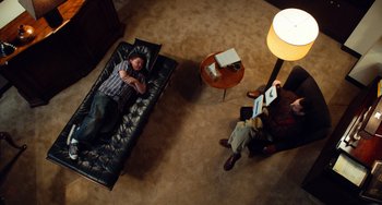 Movie still from “Superbad” (2007), directed by Greg Mottola – Two people are sitting on a black leather couch; Wide shot, Overhead angle