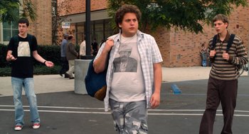 Movie still from “Superbad” (2007), directed by Greg Mottola – A man walking down a street holding a bag; Medium shot, Over the shoulder angle