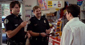 Movie still from “Superbad” (2007), directed by Greg Mottola – A police officer is smiling for the camera; Medium shot, Over the shoulder angle