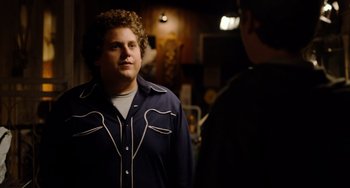 Movie still from “Superbad” (2007), directed by Greg Mottola – A man standing next to another man in a room; Medium shot, Over the shoulder angle