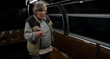 Movie still from “Superbad” (2007), directed by Greg Mottola – An older man standing on a train with his hand raised; Medium shot, Low angle