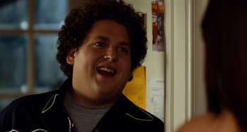 Movie still from “Superbad” (2007), directed by Greg Mottola – A man with curly brown hair is smiling for the camera; Close Up shot, Over the shoulder angle