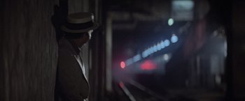 Movie still from “Superman” (1978), directed by Richard Donner – A man wearing a hat standing next to train tracks at night; Wide shot, Over the shoulder angle