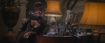 Movie still from “Superman” (1978), directed by Richard Donner – A woman standing in front of a table filled with items; Medium shot, Over the shoulder angle